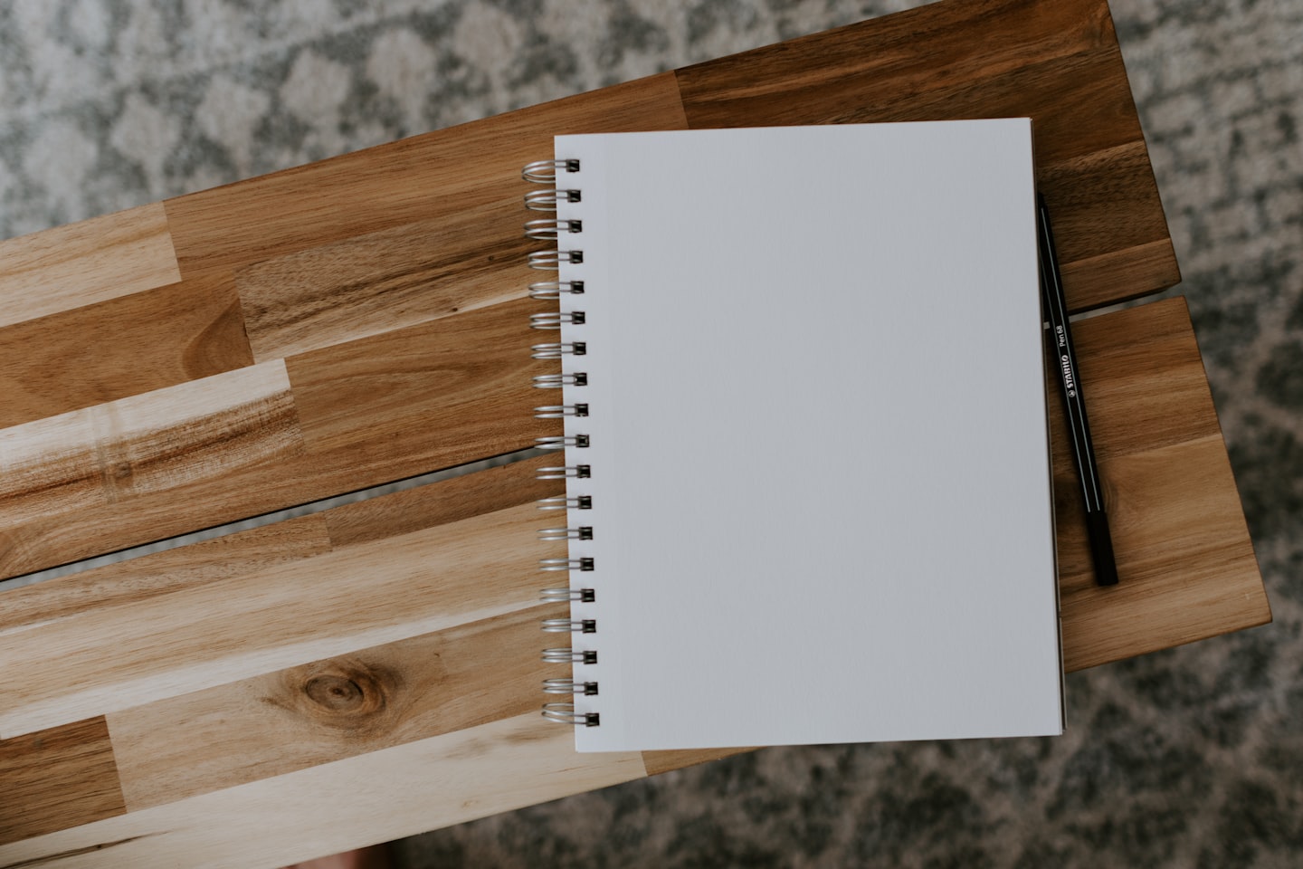 Weißes Spiralnotizbuch mit Stift auf einem Holztisch.
